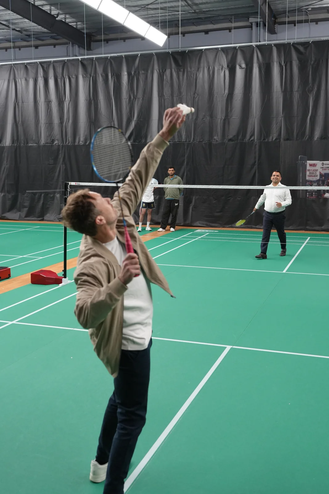 Clint reaching up with a shuttle and racket on the badminton court