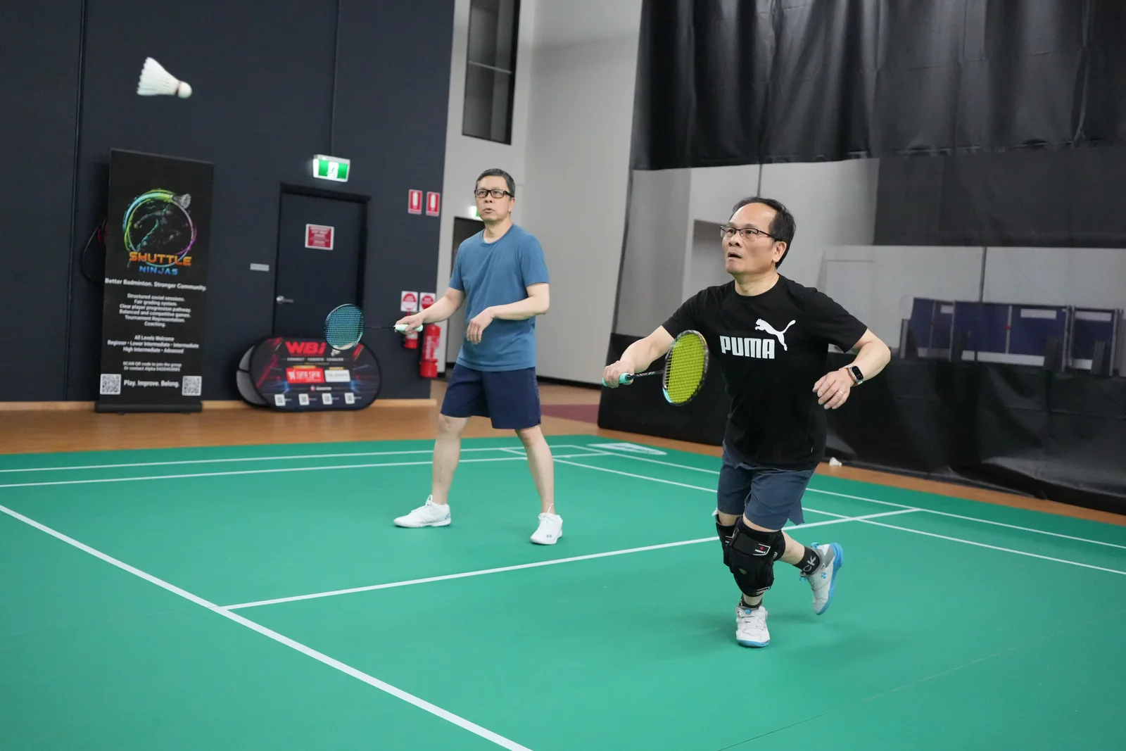 Two WBi tournament players tracking the shuttle during a doubles rally